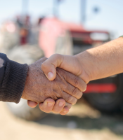 Two farmers shaking hands in front of a red tractor