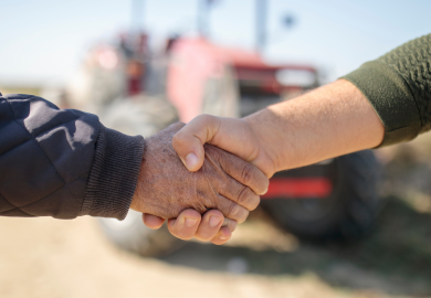 Two farmers shaking hands in front of a red tractor