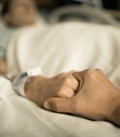 Holding elderly person's hand in hospital bed