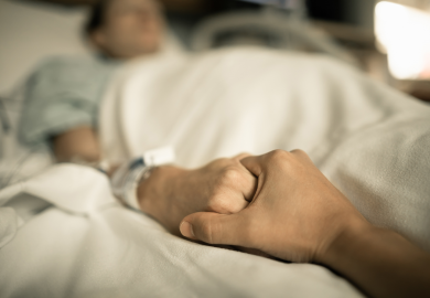 Holding elderly person's hand in hospital bed