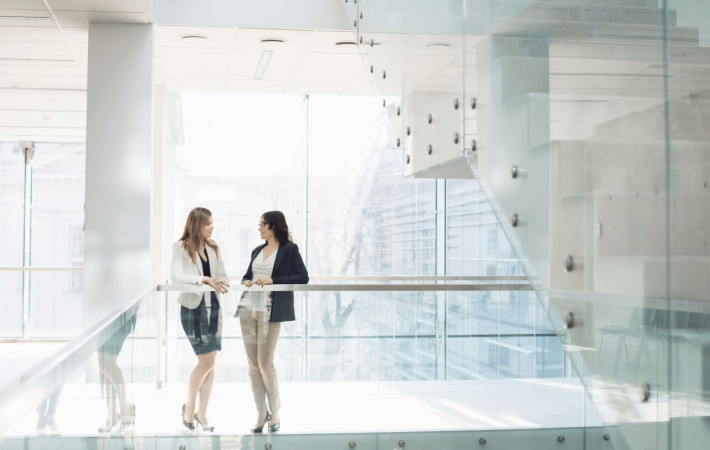 Two women stood talking on glass stairwell