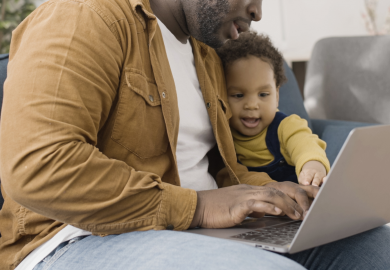 Man holding baby while working on laptop